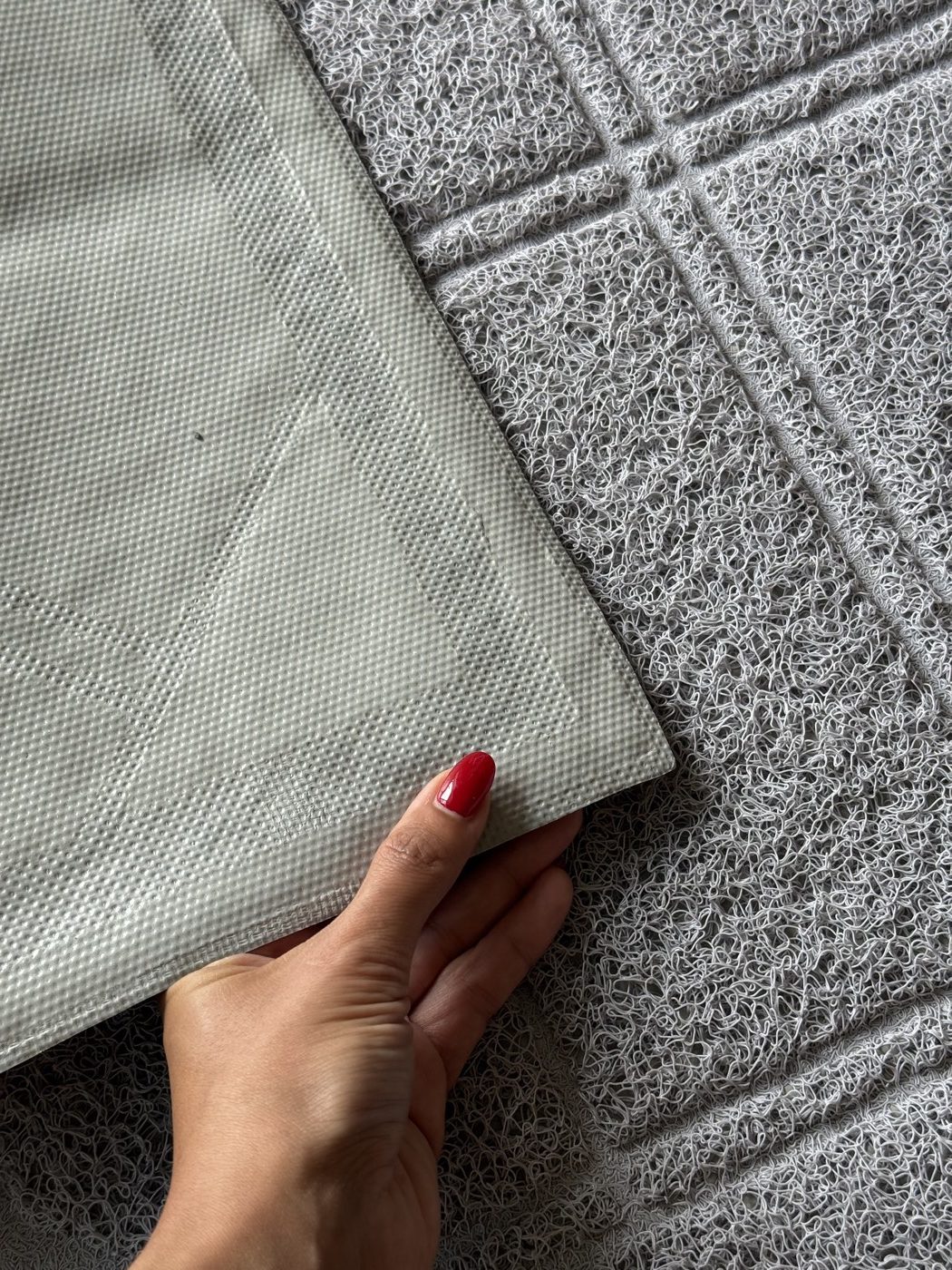 A hand lifting the mat to show its textured backing